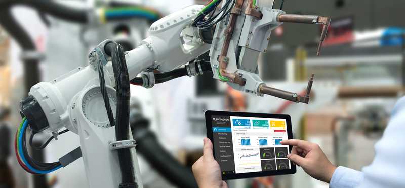 A person holding up a tablet that is controlling an industrial robot.