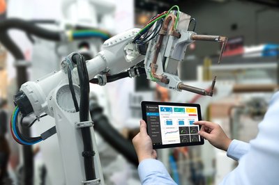A person holding up a tablet that is controlling an industrial robot.
