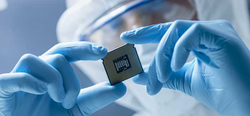 A person in a mask holding a microchip between gloved hands.