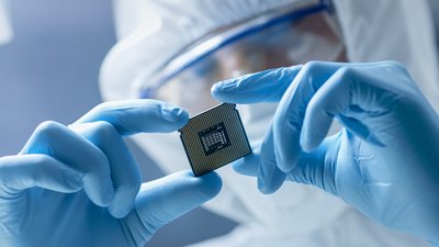 A person in a mask holding a microchip between gloved hands.