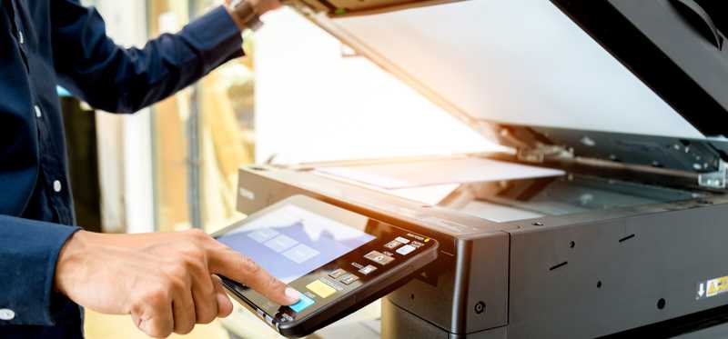 A person pressing a button on a photocopy machine.