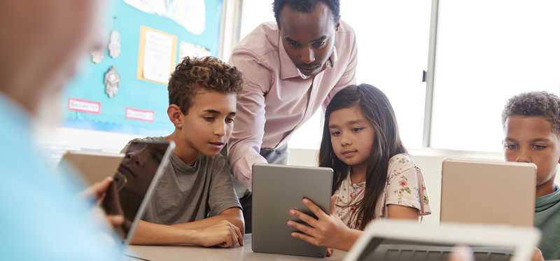 A teacher helping students holding tablets.
