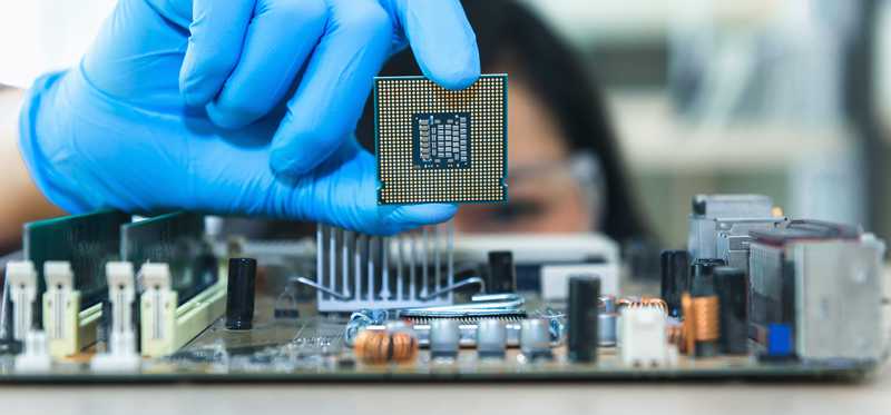 A gloved woman holding up a chip above electronics.