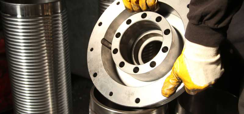 Gloved hands holding an industrial part made of aluminum.