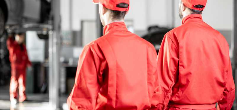 Two men in bright red uniforms in an auto shop.