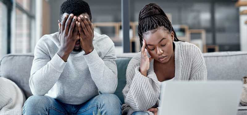 A stressed-out couple sits in front of a laptop computer.