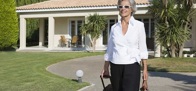 A smiling person is rolling a suitcase down the driveway of a luxury vacation home.