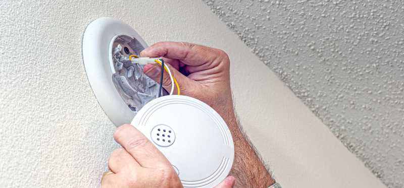 Closeup of two hands replacing a smoke detector.