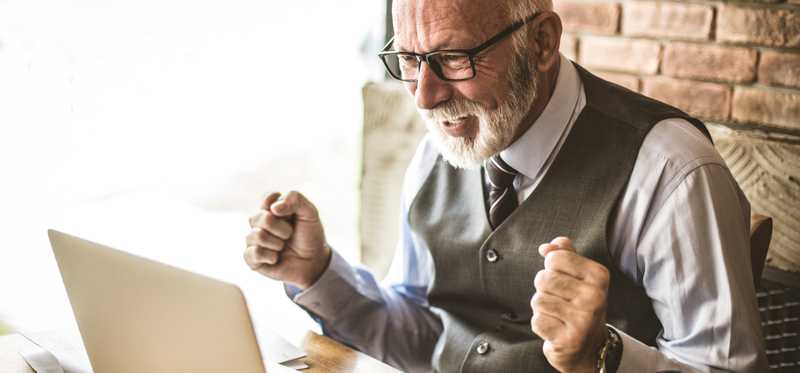 Happy person in vest celebrates while looking at laptop.
