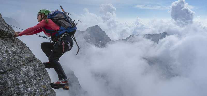 Hiker climbing mountain past clouds.