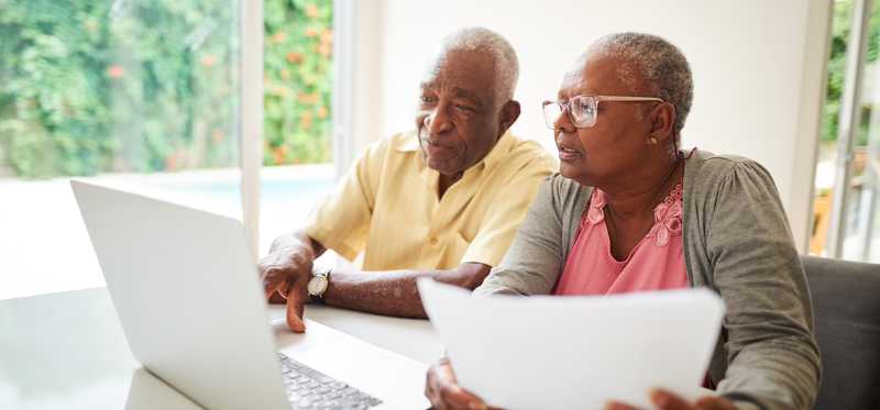 Two people looking at laptop and paperwork.