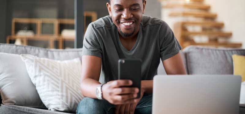 Person on couch with open laptop nearby smiles while looking at a phone.