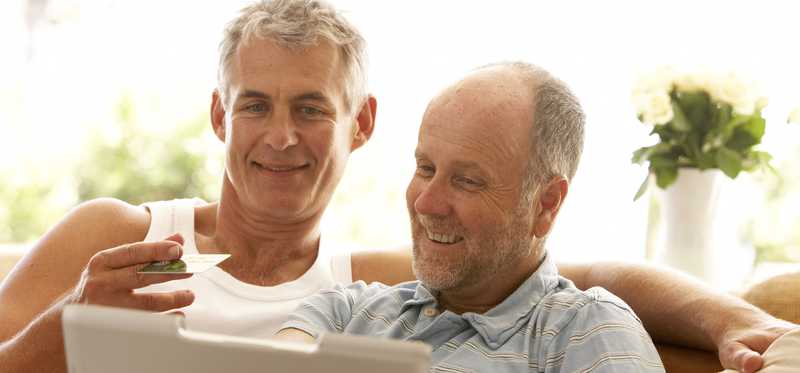 Two people smiling while using credit card online on laptop.