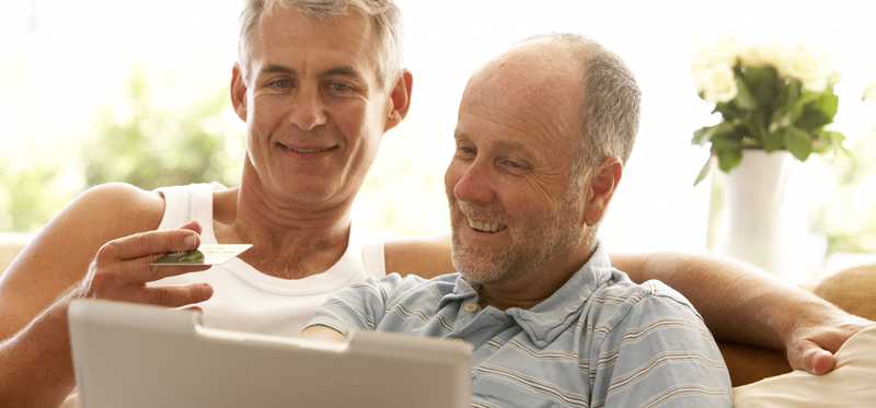 Smiling people sitting on couch holds credit card and laptop.