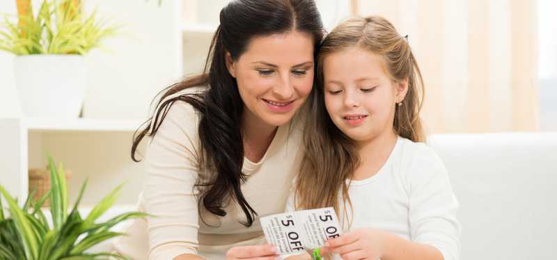 Adult and child cut coupons at coffee table.