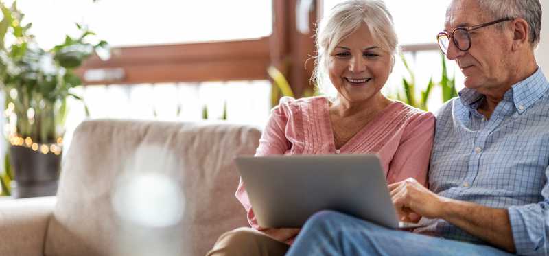 Two people sit on couch and look at laptop.