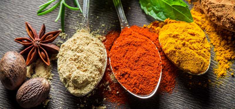 Spoonfuls of different ground spices next to whole spices.