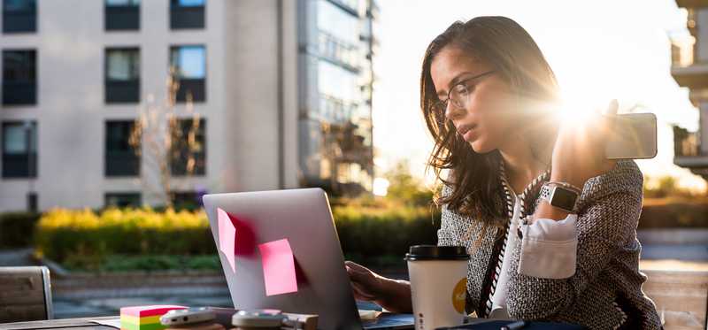 Person working outdoors with laptop, phone, and headphones.
