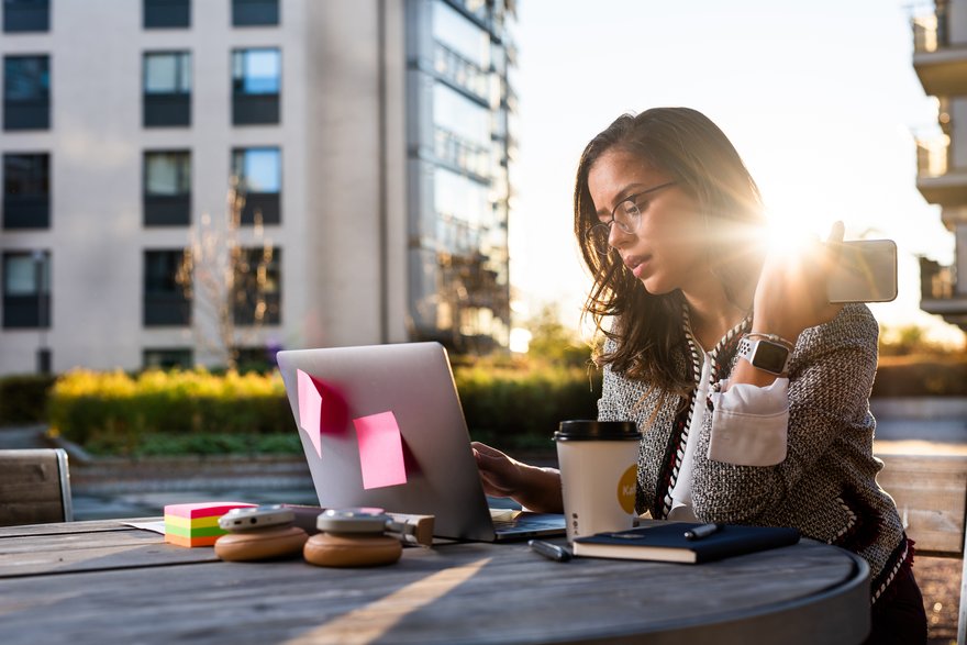 Man working outdoors using laptop, phone and headphones.