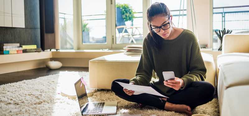 Person wearing glasses sits on floor and reviews paperwork thoughtfully.