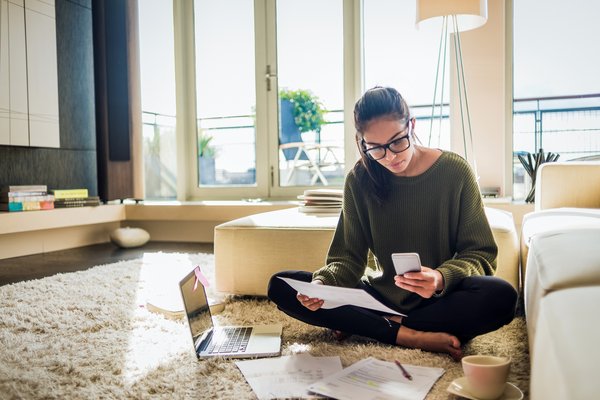 Person wearing glasses sits on floor and reviews paperwork thoughtfully.