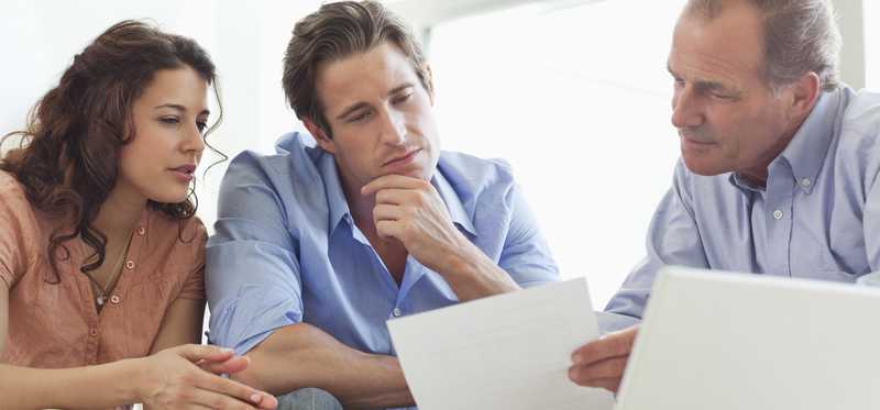 Young couple sits with adult male looking at paperwork.