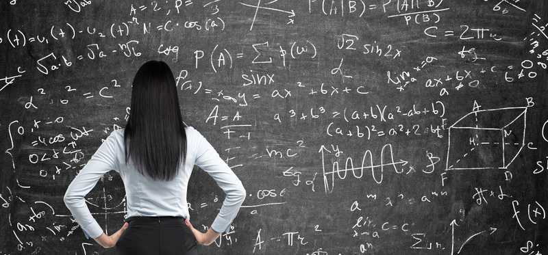 Person with hands on hips and looking at a blackboard full of math formulas.