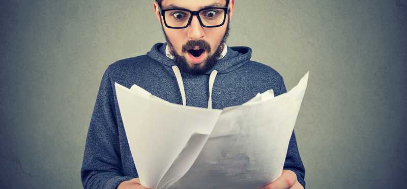 Surprised man in glasses with beard looking at papers in his hands.