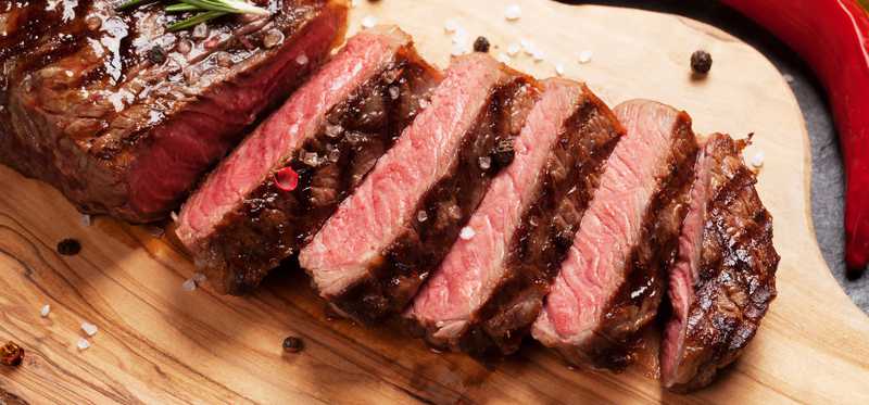A steak cut up on a wooden cutting board.