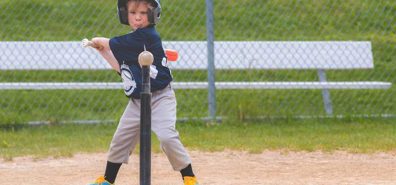 A small child hitting a baseball off of a tee.