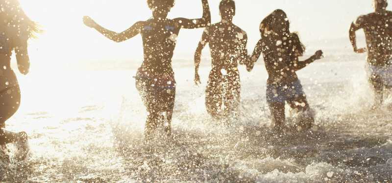People in the surf at a beach with the sun behind them
