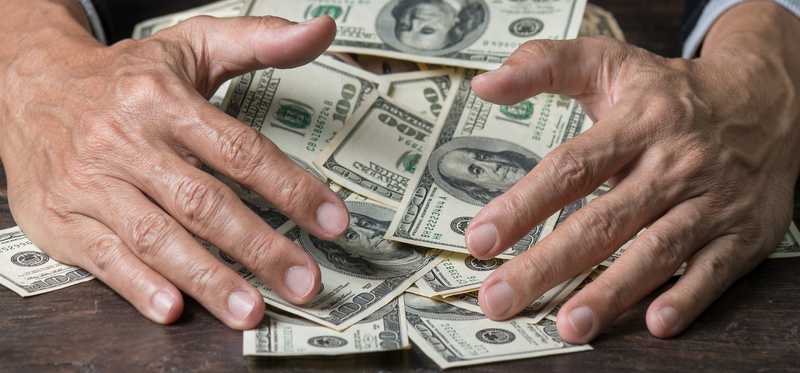 Person pulling a pile of hundred dollar bills toward themself.