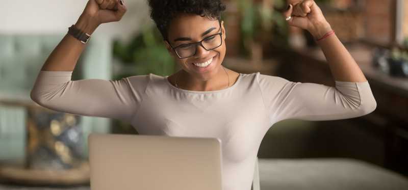 A person raising arms in triumph in front of a computer.