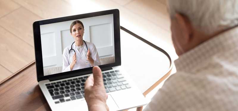 An older man talking over video chat on a laptop with a physician