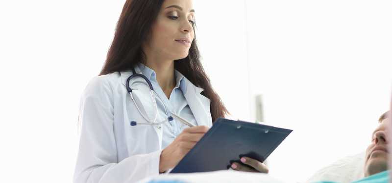 A female doctor standing over a male patient in a bed.
