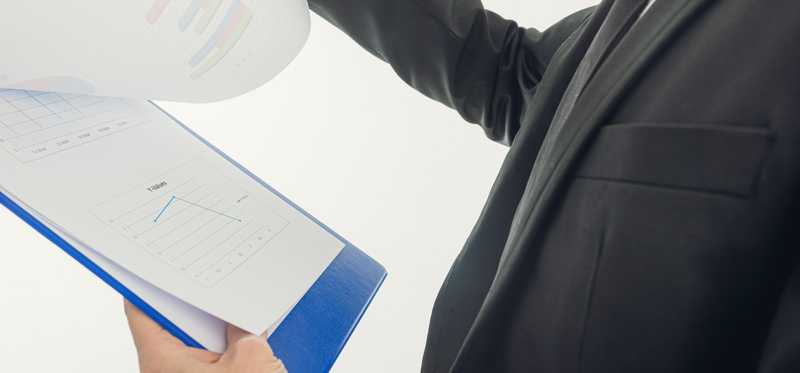 A man in a suit looking over paperwork on a clipboard.