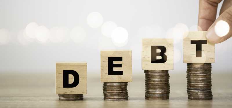 Rising stacks of coins with blocks atop spelling out Debt.