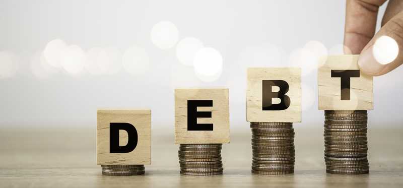 Rising stacks of coins with blocks atop spelling out DEBT