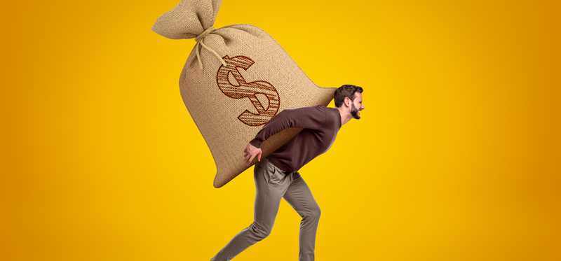 A man carrying a giant bag with a dollar sign on his back.