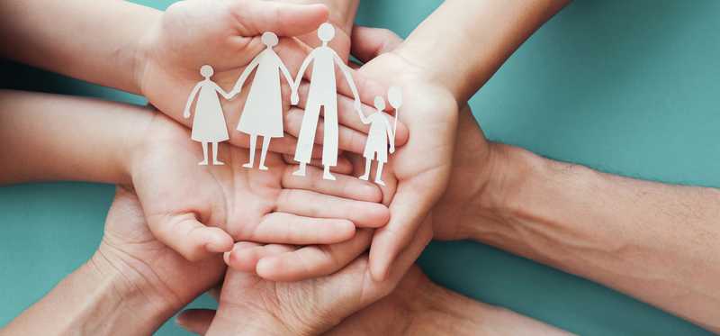 Four pairs of hands holding a paper cut out family.