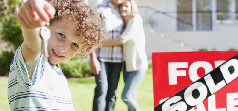 Family standing in front of a house with a Sold sign in the yard.