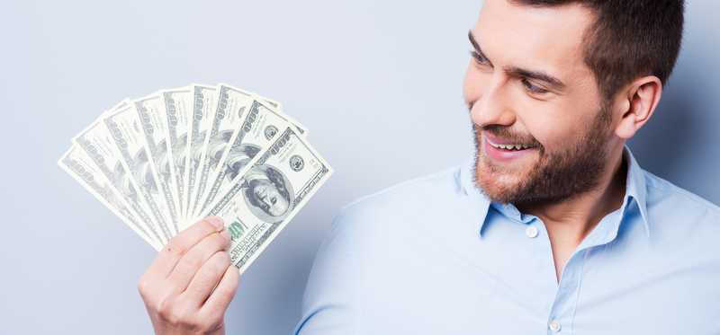 Man smiling as he holds a fanned pile of money in one hand.