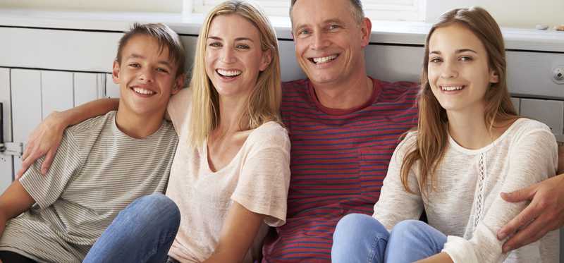 Family sits together smiling on a couch.