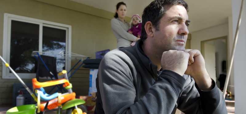 Person sits in thought with adult and infant behind.
