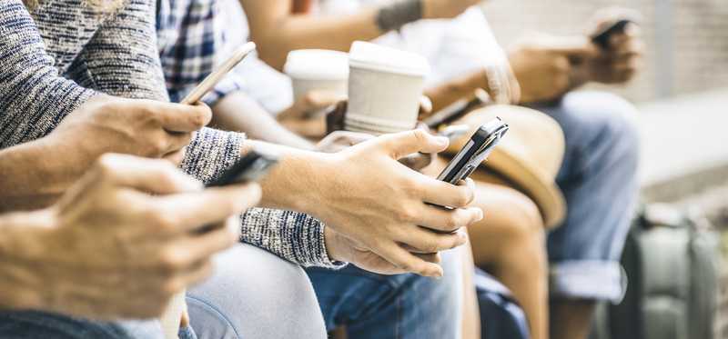 Group of people holding cups of coffee and using their cell phones.