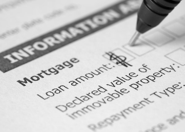 A hand holding a pen and writing in the loan amount on a mortgage application.