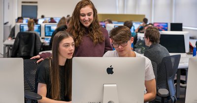 Teens looking at Mac computer in classroom