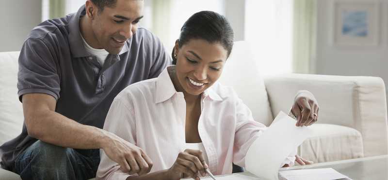 Person sitting on floor shows paperwork on table to person on couch.