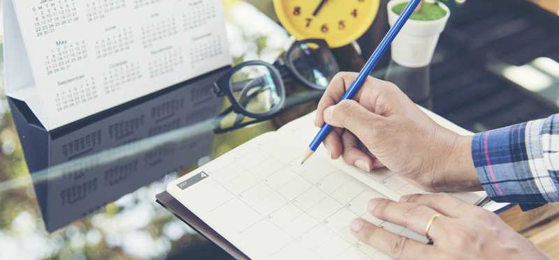 Person writing in appointment book next to clock.