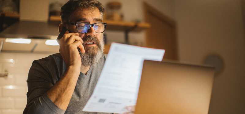 Person reviewing paperwork while talking on phone.